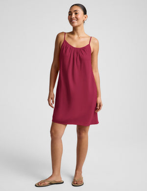 Woman wearing a magenta cupro mini dress and brown sandals against a plain background. 