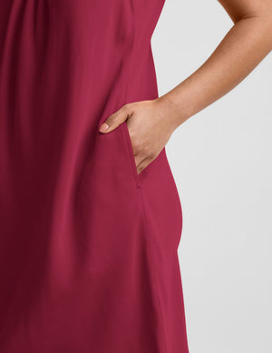 Woman wearing a magenta cupro mini dress and brown sandals against a plain background. 