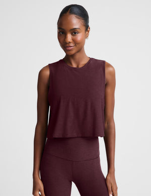 A woman modeling a sleeveless cropped tank top and matching leggings in a deep burgundy color, set against a plain light gray studio background.