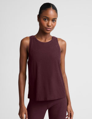 A woman modeling a sleeveless heathered burgundy tank top and matching leggings against a light gray studio background.