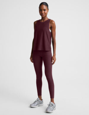 A woman modeling a sleeveless heathered burgundy tank top and matching leggings against a light gray studio background.