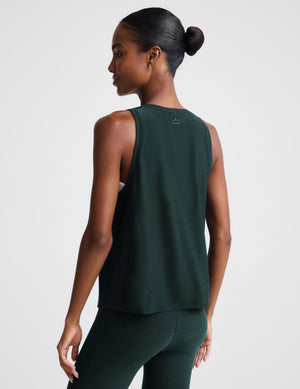 Woman wearing a green tank top and matching leggings against a plain studio background. 
