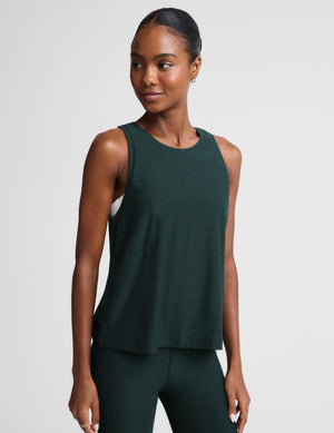 Woman wearing a green tank top and matching leggings against a plain studio background. 