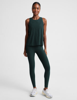 Woman wearing a green tank top and matching leggings against a plain studio background. 