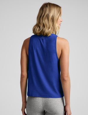 A woman wearing a blue tank top and gray biker shorts against a plain studio background. 