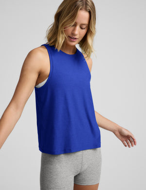 A woman wearing a blue tank top and gray biker shorts against a plain studio background. 