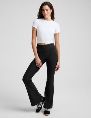 A woman wearing a fitted white short-sleeve crop top and black leggings, photographed against a plain light gray studio background.