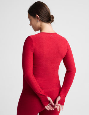 Pregnant woman wearing a red long sleeve top and leggings against a plain background. 