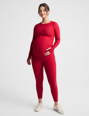 Pregnant woman wearing a red long sleeve top and leggings against a plain background. 