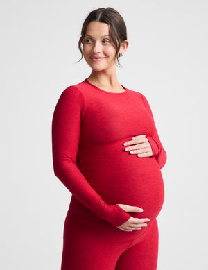 Pregnant woman wearing a red long sleeve top and leggings against a plain background. 