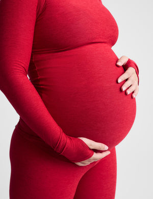 Pregnant woman wearing a red long sleeve top and leggings against a plain background. 