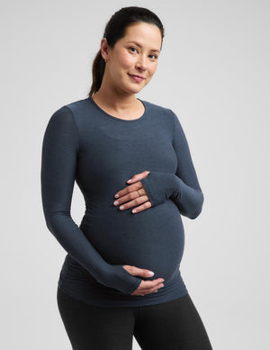 Pregnant woman wearing a blue maternity long sleeve top and black maternity leggings against a plain background. 