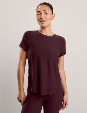 A woman wearing a short sleeve burgundy t-shirt and matching leggings against a plain studio background. 