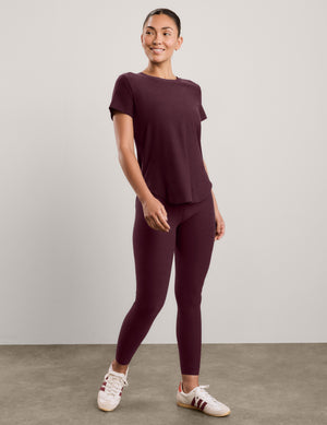 A woman wearing a short sleeve burgundy t-shirt and matching leggings against a plain studio background. 