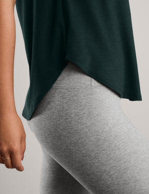 Woman wearing a green short sleeve t-shirt and gray capri leggings against a plain background. 