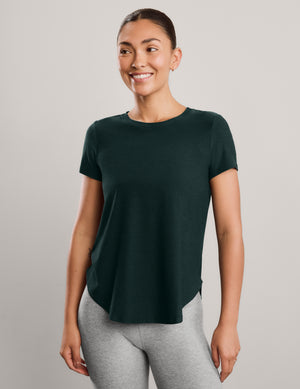 Woman wearing a green short sleeve t-shirt and gray capri leggings against a plain background. 