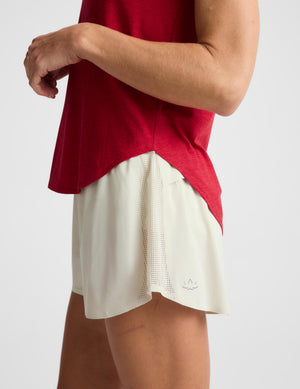 A woman wearing a bright red short-sleeve athletic top and light cream shorts against a light gray studio background.