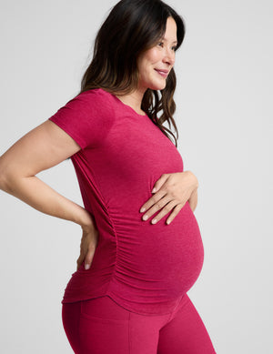 Pregnant woman wearing a red maternity t-shirt and shorts against a plain background. 
