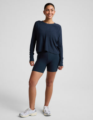 A woman modeling a dark navy blue long-sleeve crop top and matching high-waisted bike shorts against a light gray studio background.