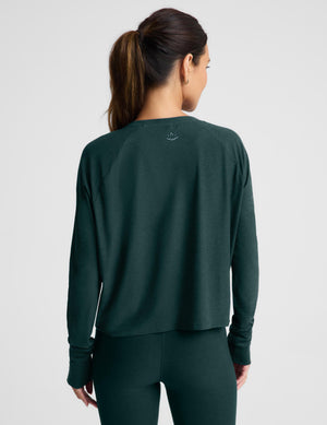 A woman modeling a dark forest green long-sleeve cropped top and matching leggings against a light gray studio background.