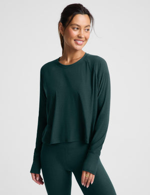 A woman modeling a dark forest green long-sleeve cropped top and matching leggings against a light gray studio background.