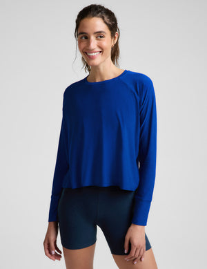 A woman modeling a royal blue long-sleeve athletic top with raglan sleeves and dark navy fitted shorts against a light gray studio background.