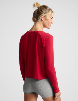 A woman wearing a bright red long sleeve and gray biker shorts against a plain background. 