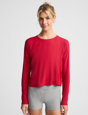 A woman wearing a bright red long sleeve and gray biker shorts against a plain background. 