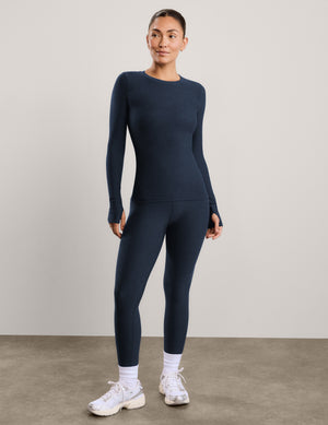 A woman modeling a dark navy blue long-sleeve crewneck top and matching leggings against a plain light gray studio background.