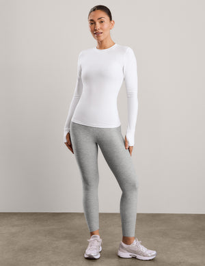 A woman modeling a fitted white long-sleeve crewneck athletic top against a plain light gray studio background.