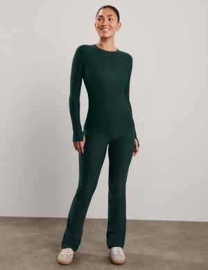A woman modeling a dark forest green long-sleeve crewneck top and matching pants against a neutral light gray studio background.