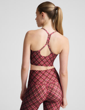 A woman modeling a matching athletic set featuring a red and pink plaid sports bra and high-waisted leggings against a light gray studio background.