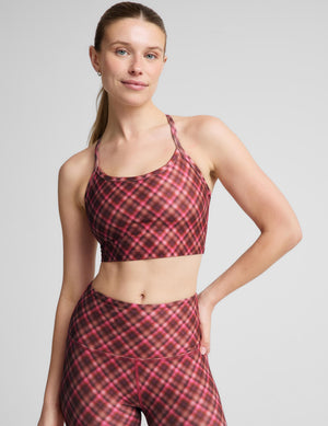A woman modeling a matching athletic set featuring a red and pink plaid sports bra and high-waisted leggings against a light gray studio background.