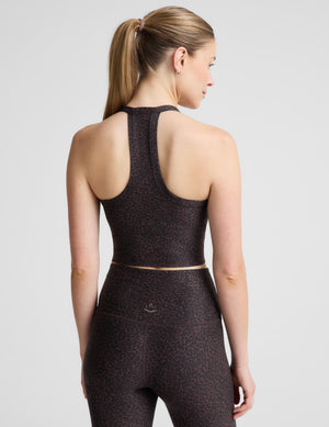 A woman modeling a matching activewear set featuring a dark brown and black leopard print cropped tank and high-waisted leggings, set against a plain light gray background.