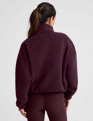 A woman wearing a dark burgundy boucle zip-up jacket and matching leggings, posing against a light gray studio background.