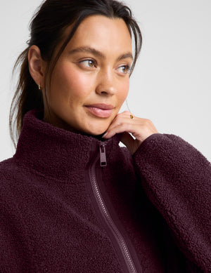 A woman wearing a dark burgundy boucle zip-up jacket and matching leggings, posing against a light gray studio background.