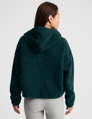 A woman wearing a dark green fleece half-zip pullover sweater and light gray leggings, standing against a light gray studio background.