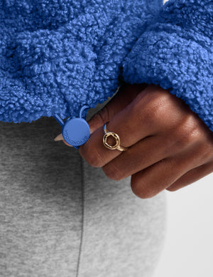 A woman wearing a textured blue fleece quarter-zip pullover sweater and gray leggings, posing against a light gray studio background.