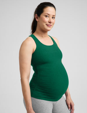 Pregnant woman wearing a green maternity racerback tank and gray leggings against a plain background. 