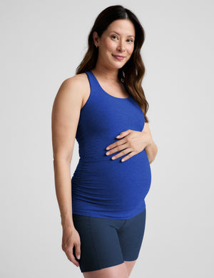 A pregnant woman wearing a royal blue maternity tank top and dark navy biker shorts, standing against a light gray studio background.