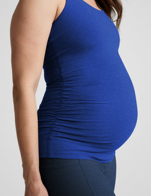 A pregnant woman wearing a royal blue maternity tank top and dark navy biker shorts, standing against a light gray studio background.