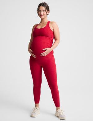 Pregnant woman wearing a red maternity tank top and red maternity leggings against a plain background. 