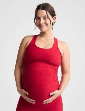 Pregnant woman wearing a red maternity tank top and red maternity leggings against a plain background. 