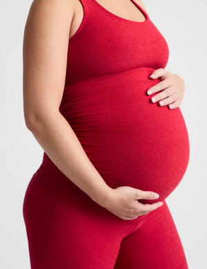 Pregnant woman wearing a red maternity tank top and red maternity leggings against a plain background. 