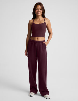 A woman modeling a matching athletic set consisting of a dark burgundy cropped tank top and matching sweatpants against a light gray studio background.