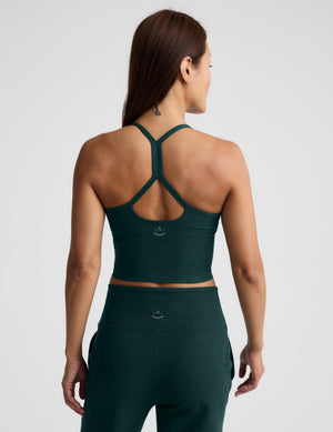 A woman wearing a dark forest green athletic crop top and matching high-waisted pants against a light gray studio background.