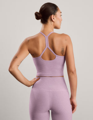 A woman modeling a matching light purple athletic set consisting of a scoop-neck cropped tank and high-waisted leggings, posed against a solid light gray background.