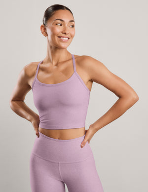 A woman modeling a matching light purple athletic set consisting of a scoop-neck cropped tank and high-waisted leggings, posed against a solid light gray background.