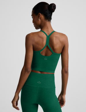 Woman wearing a green cropped racerback tank and leggings against a plain background. 