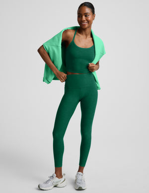 Woman wearing a green cropped racerback tank and leggings against a plain background. 